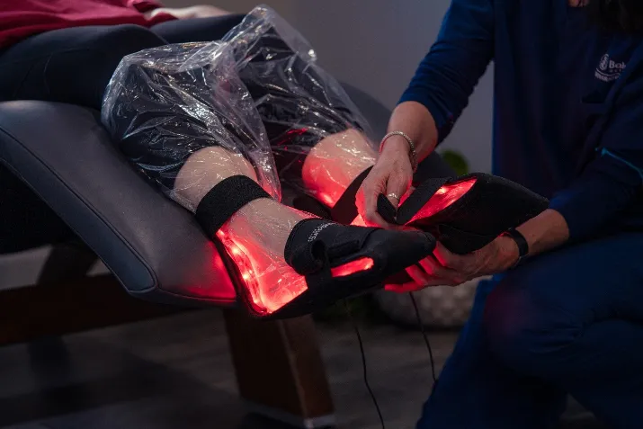 Patient receiving low-level light therapy on legs with red light device to reduce pain